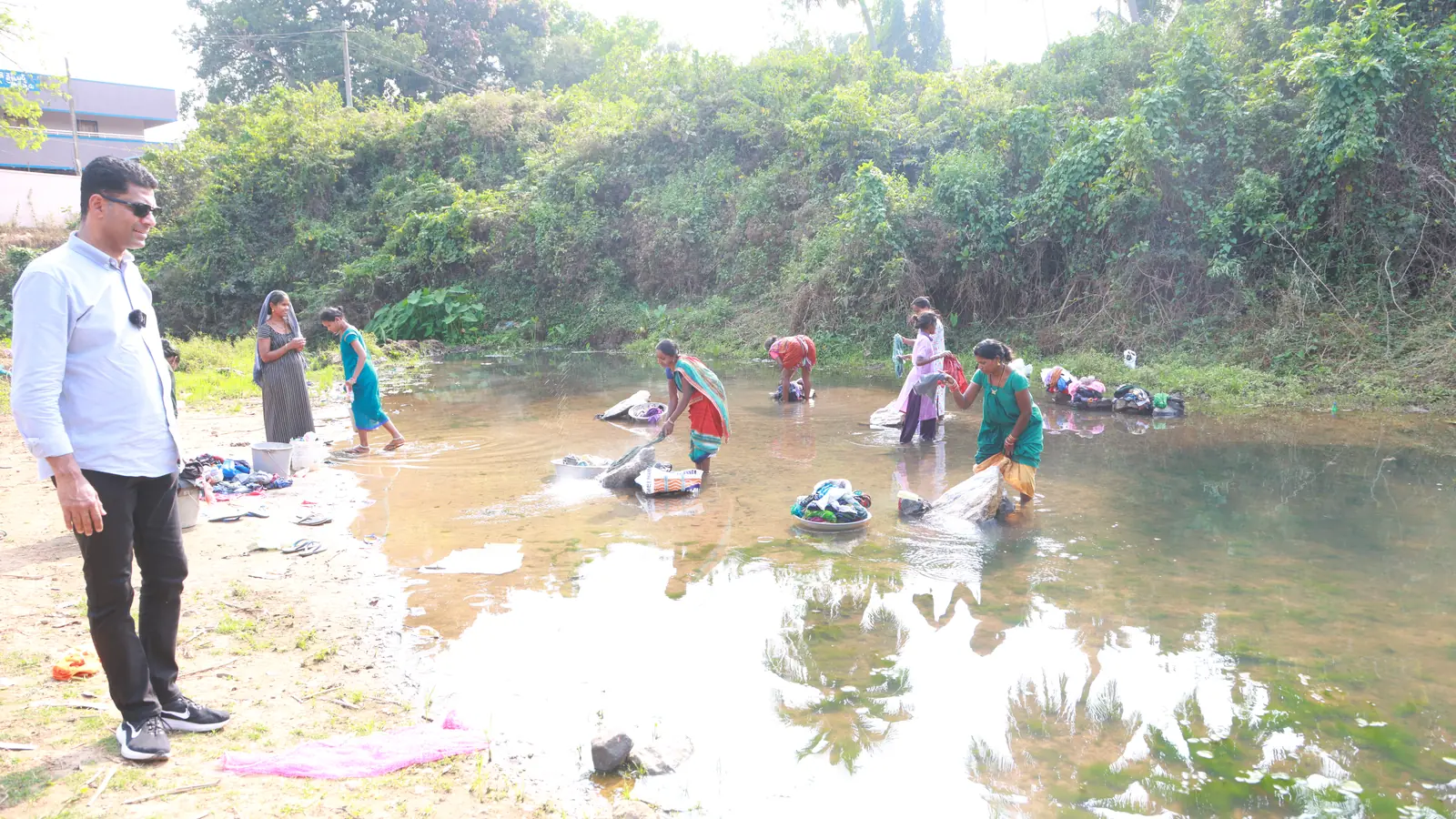 Abraham Thomas stands near women collecting water at a rural water source.