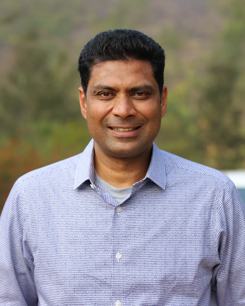 Abraham Thomas, founder of Breakthrough Water, smiling outdoors with wooded hills behind him.