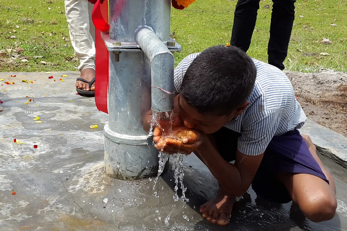 A child drinks flowing water from a village hand pump.