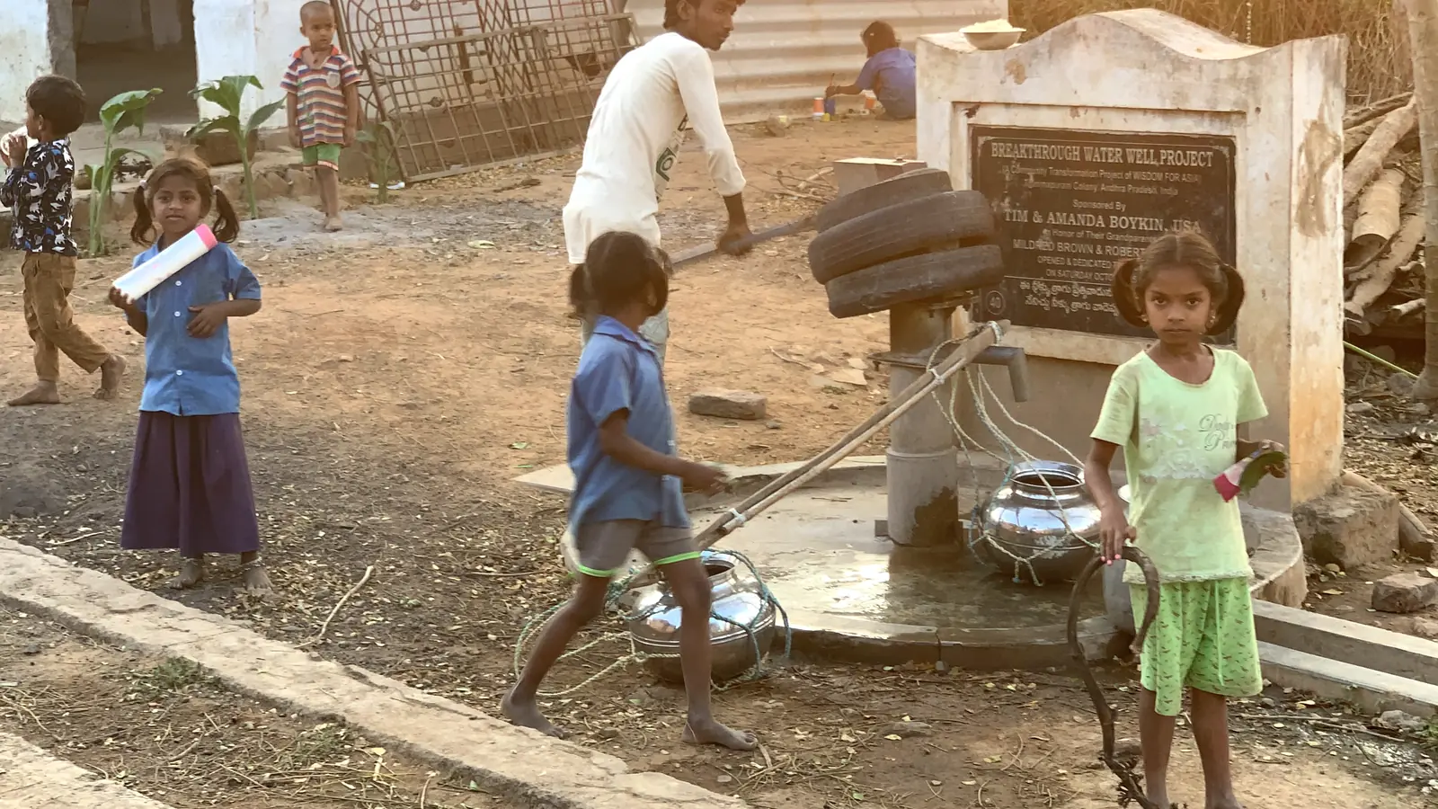Children carry water containers beside a village hand pump photographed after several years of use.