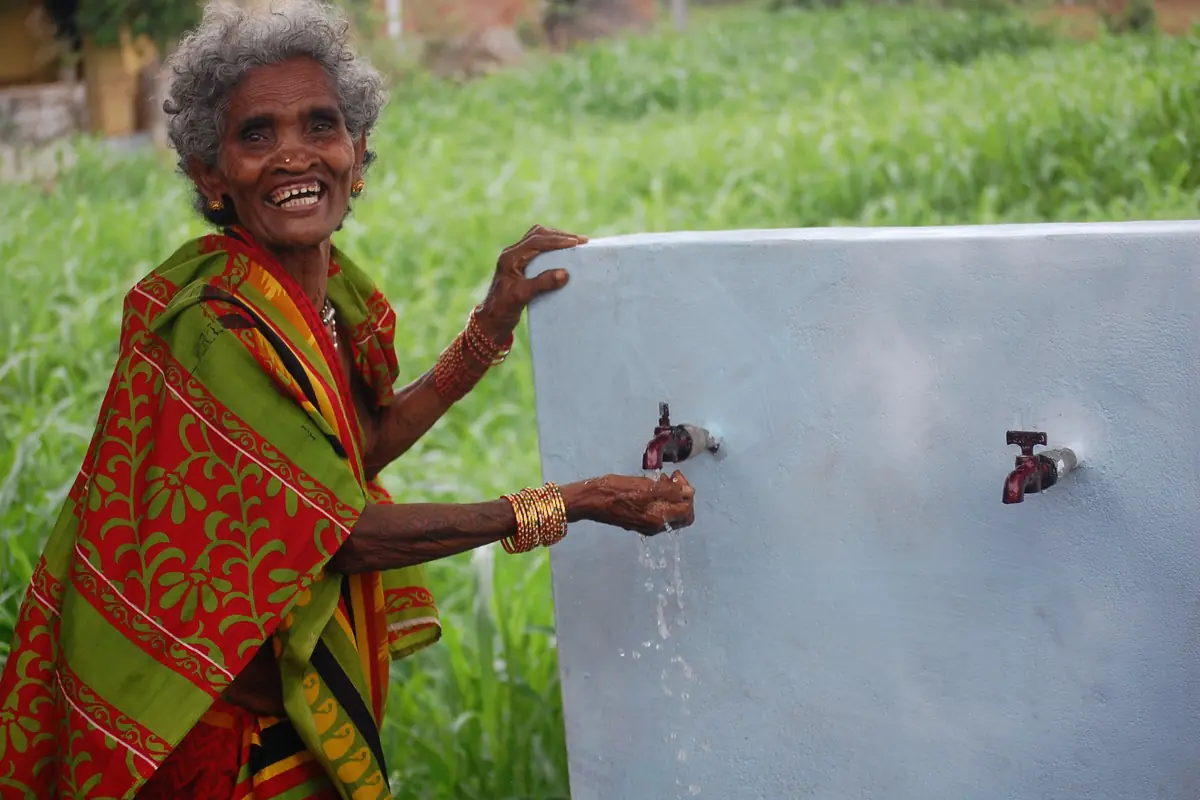 A woman smiles beside a flowing tap at a Breakthrough Water school water-distribution project.
