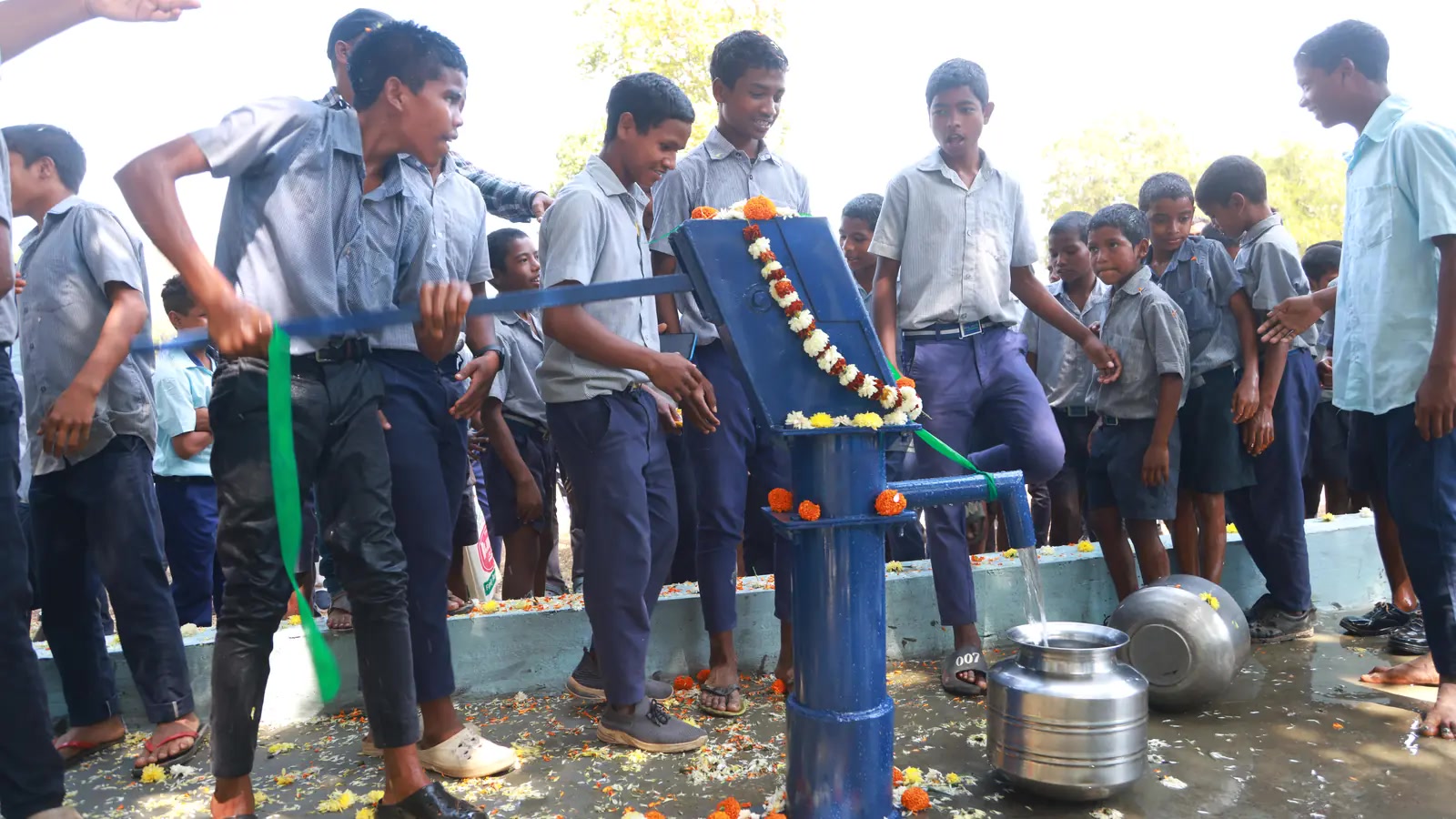 Schoolchildren gather around a hand pump at their school.